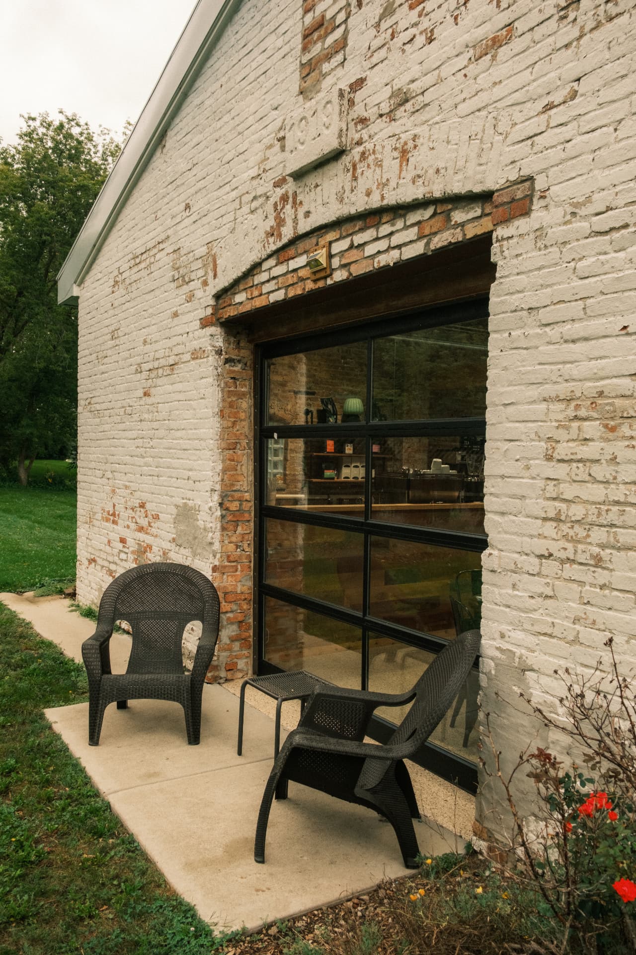 Patio chairs beside DSCO Coffee's original white brick exterior and glass garage door