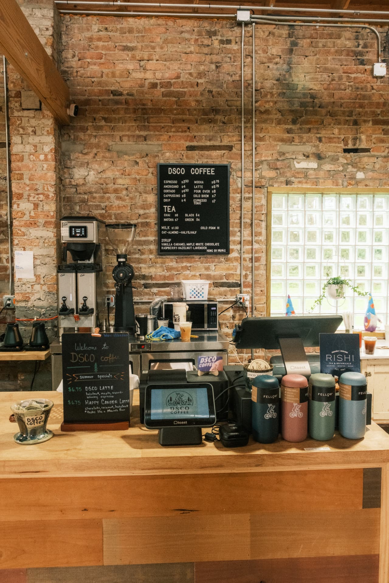 The DSCO Coffee counter with the menu board, drinkware, and exposed brick wall