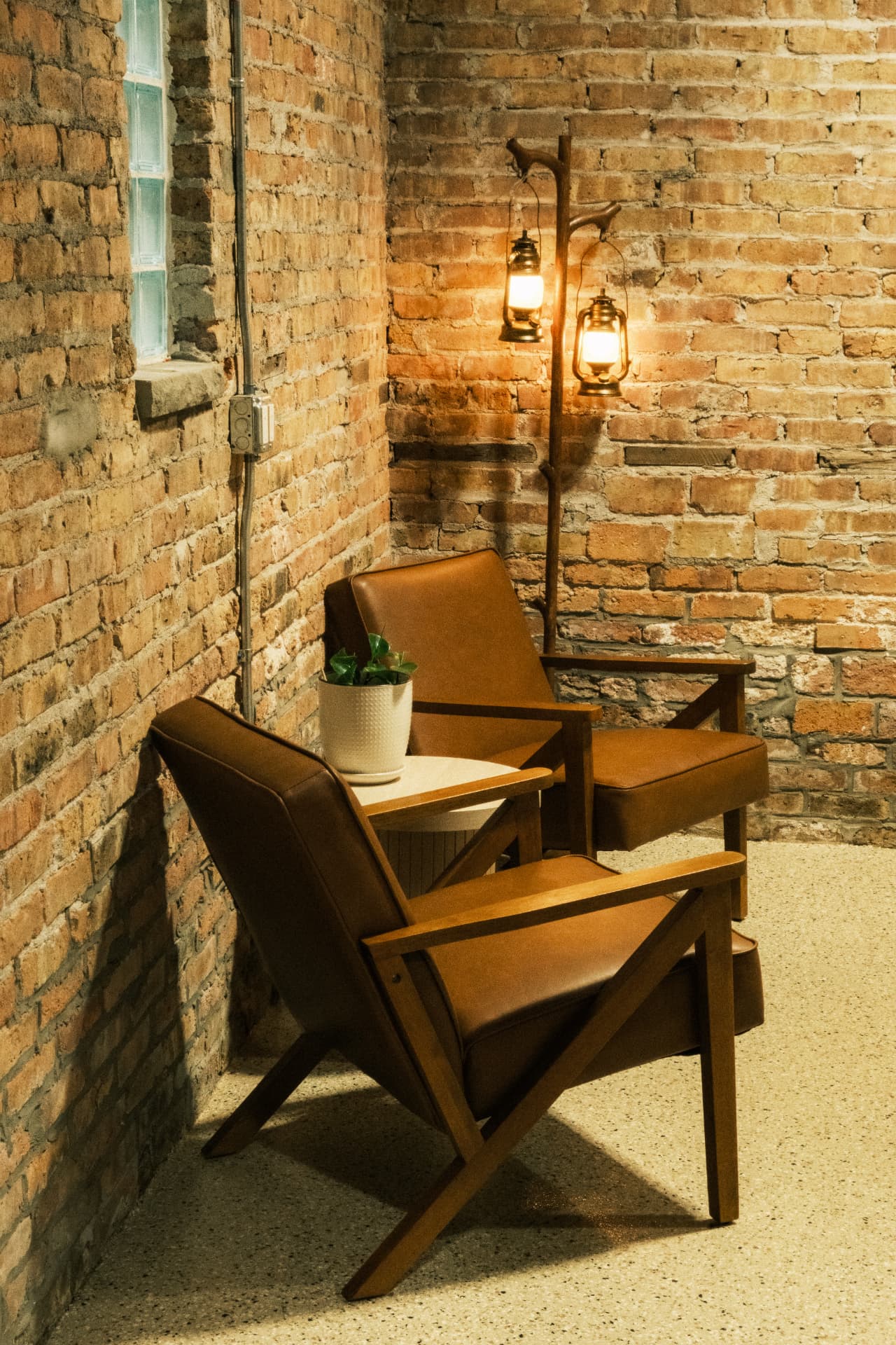 Two leather chairs and a small table beneath glowing lanterns against original brick
